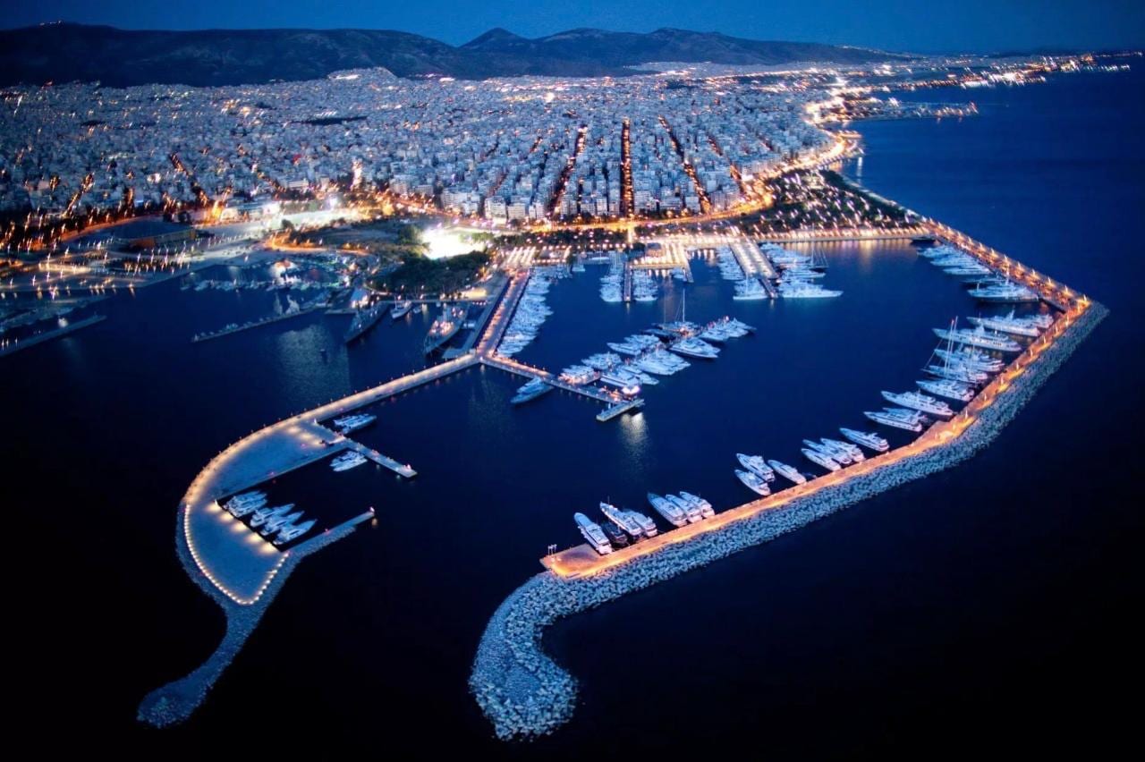 Blue-hour aerial of an Athens Riviera marina, its moored yachts and the lit city beyond