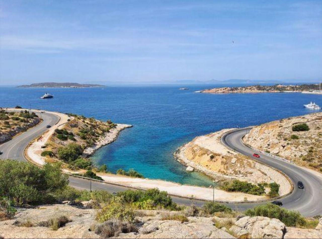 The coast road curving past a turquoise cove on the way to Cape Sounion