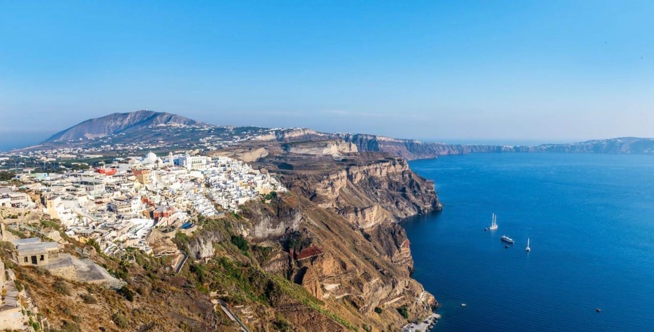 Fira spread along the caldera rim with sailing boats on the Aegean far below