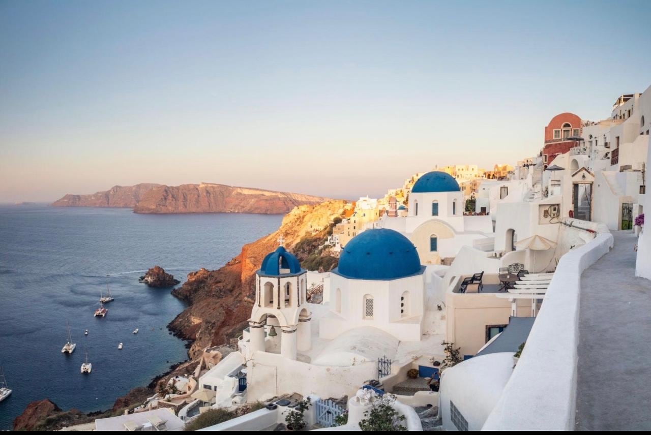 The blue domes and white cave houses of Oia at golden hour above the Santorini caldera